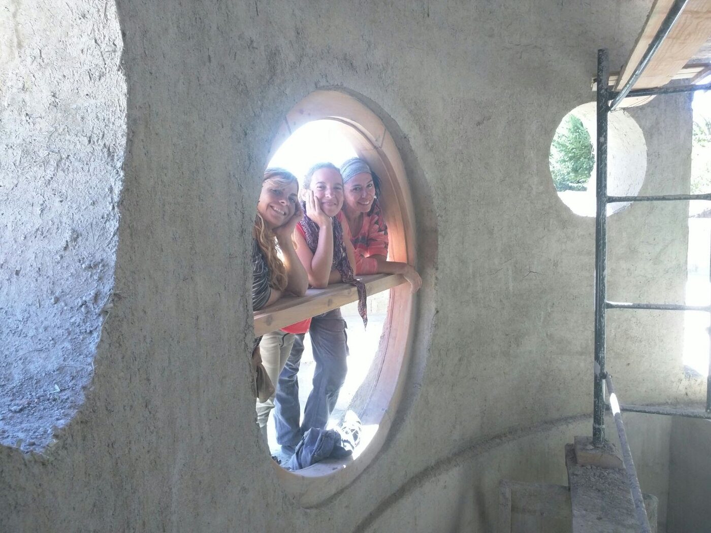 Tres personas asomadas sonriendo en una ventana ovalada